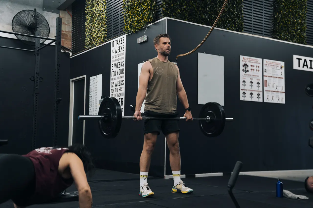 Coach deadlifting in front of the studio signage