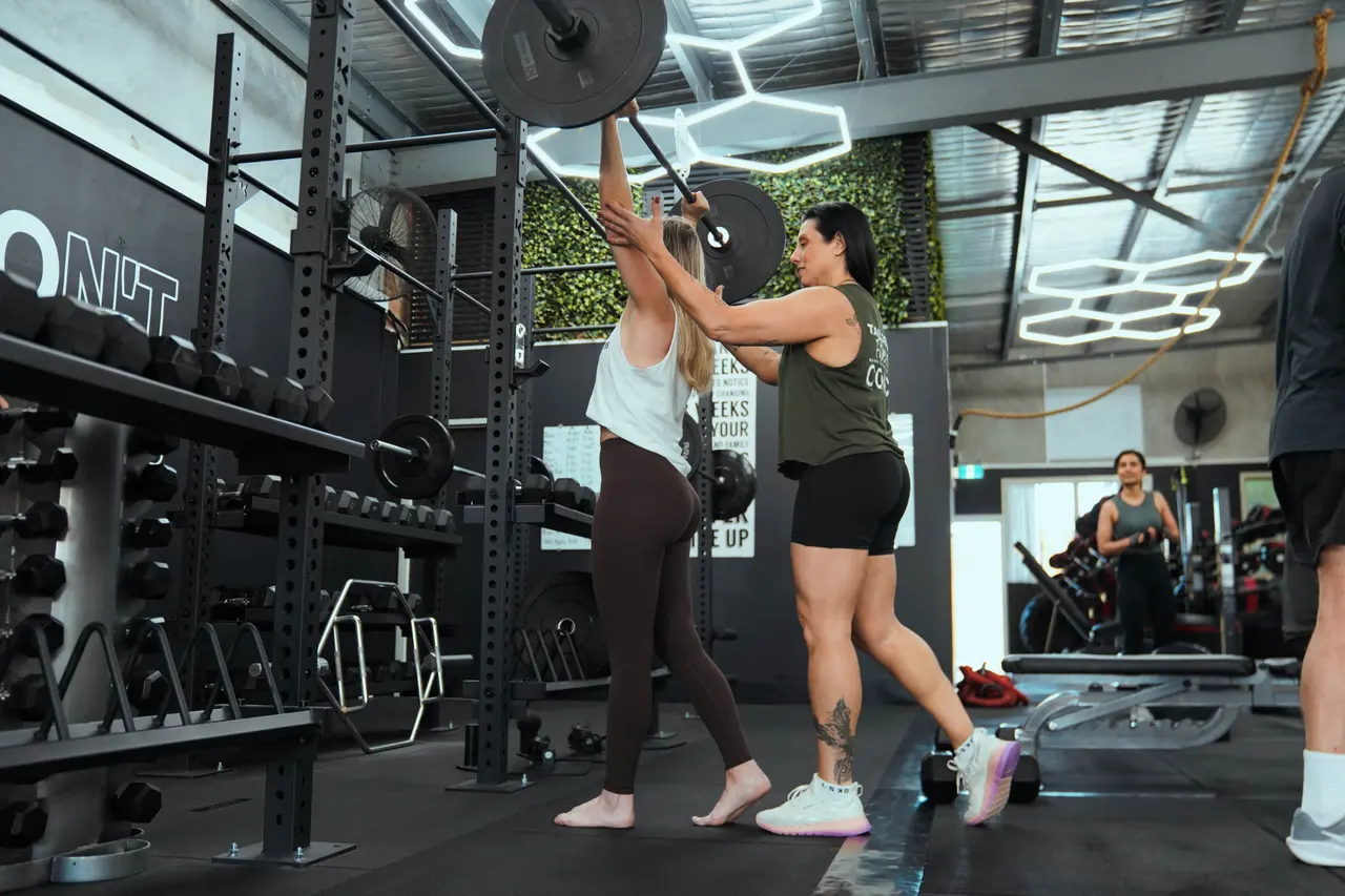 Coach assisting a member through an overhead barbell press
